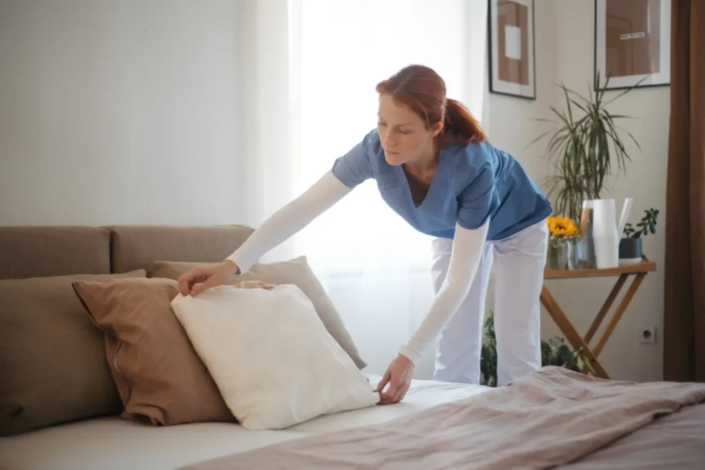 A supportive in-home caregiver in Maryland makes the bed in a senior patient's room as part of light housekeeping services.